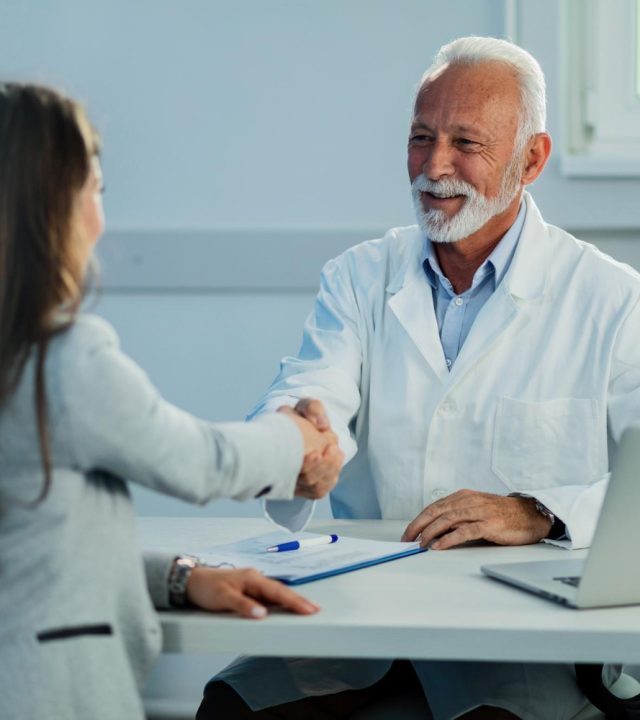 happy-mature-doctor-his-female-patient-shaking-hands-after-medical-appointment-clinic